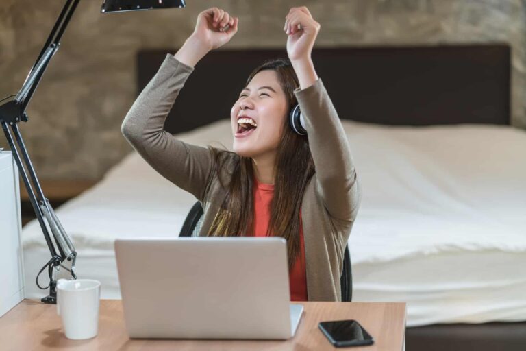 Joyful woman using headphones celebrating at laptop desk
