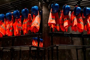 Row of orange safety vests and blue helmets hanging in industrial setting
